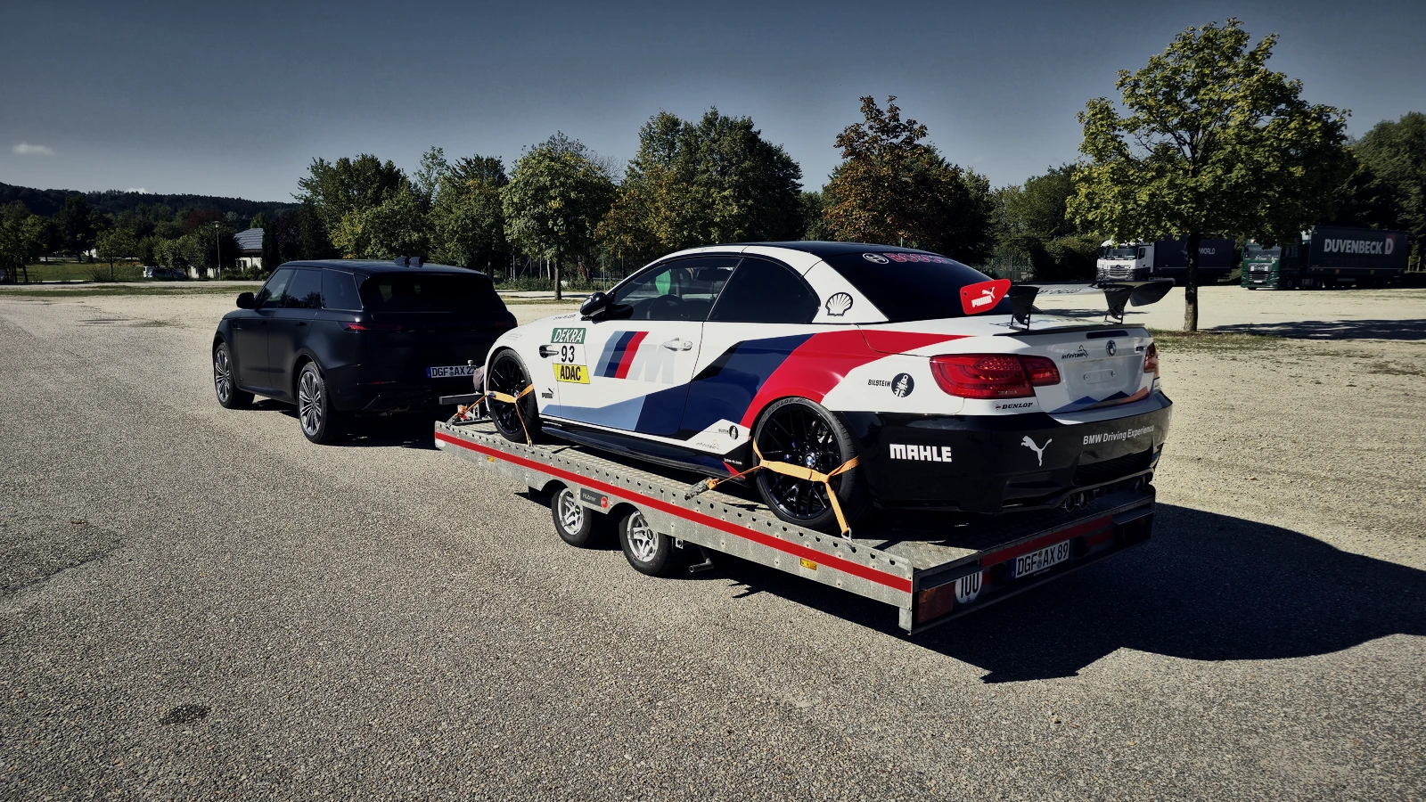 BMW M3 GT4 mit Radgurten auf der offenen Plattform, davor der Range Rover als Zugfahrzeug