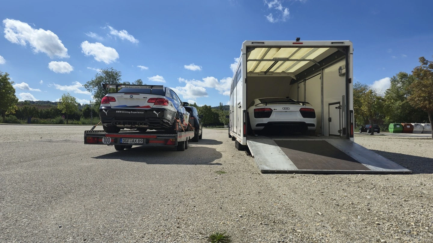 BMW M3 auf der offenen Plattform neben dem geschlossenen Anhänger mit Audi R8
