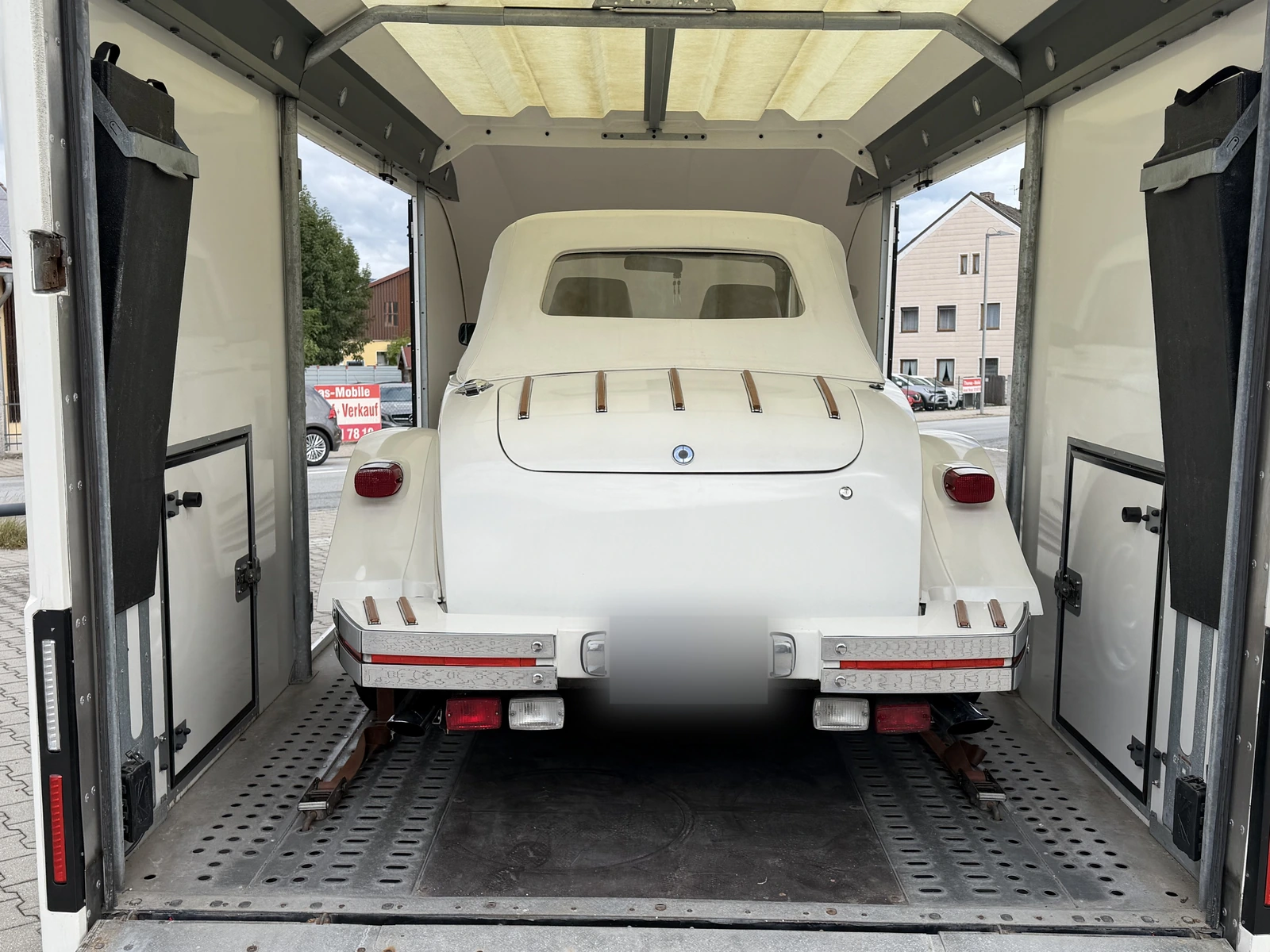 Heck eines weißen Oldtimers im geschlossenen Anhänger, Blick von hinten durch die offene Rampe